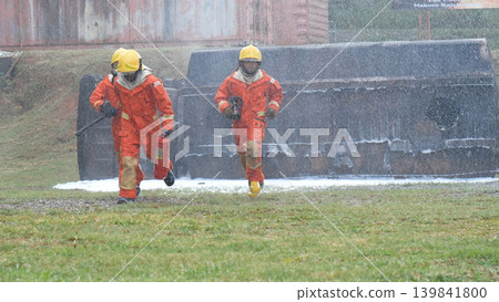 Firefighter Rescue team training in fire fighting extinguisher. Firefighter teamwork fighting with flame using fire hose chemical water foam spray engine. Fireman wear hard hat, safety suit uniform Firefighter Rescue team training in fire fighting extinguisher. Firefighter teamwork fighting with flame using fire hose chemical water foam spray engine. Fireman wear hard hat, safety suit uniform 139841800