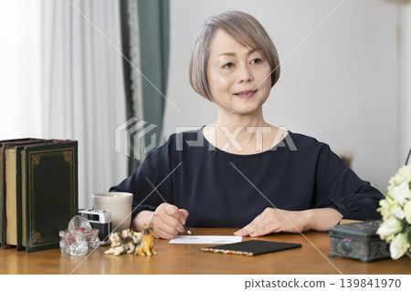 一位老婦人在客廳畫明信片。 139841970
