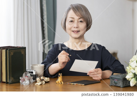 一位老婦人在客廳畫明信片。 139841980
