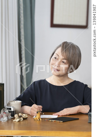 一位老婦人在客廳畫明信片。 139841987