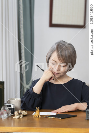 A senior woman paints picture postcards in her living room. A senior woman paints picture postcards in her living room. 139841990
