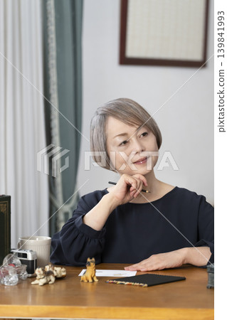 A senior woman paints picture postcards in her living room. A senior woman paints picture postcards in her living room. 139841993