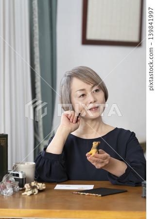 A senior woman paints picture postcards in her living room. A senior woman paints picture postcards in her living room. 139841997
