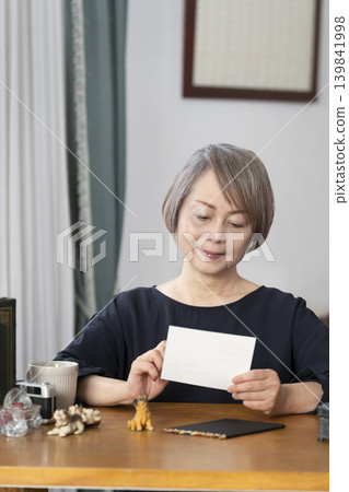 A senior woman paints picture postcards in her living room. A senior woman paints picture postcards in her living room. 139841998