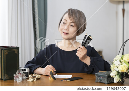 A senior woman paints picture postcards in her living room. A senior woman paints picture postcards in her living room. 139842007