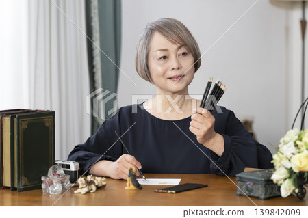 一位老婦人在客廳畫明信片。 139842009