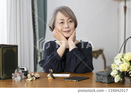 A senior woman paints picture postcards in her living room. A senior woman paints picture postcards in her living room. 139842017