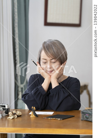 A senior woman paints picture postcards in her living room. A senior woman paints picture postcards in her living room. 139842022