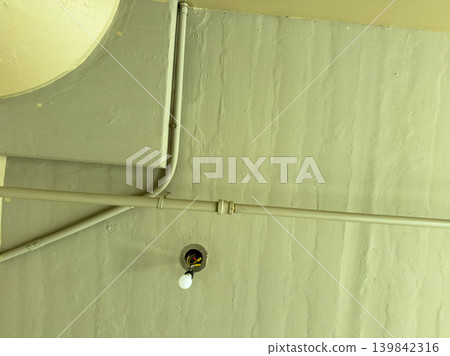 Pipes and light bulb on ceiling in a room during daytime with natural light coming through Pipes and light bulb on ceiling in a room during daytime with natural light coming through 139842316