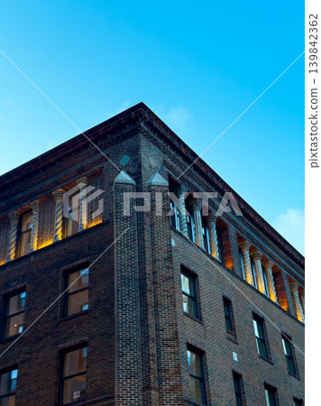 Building corner shows brick work and windows against clear blue sky during evening light Building corner shows brick work and windows against clear blue sky during evening light 139842362