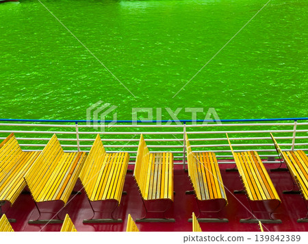 Bright green water and empty benches on a boat during daylight in a lively river setting 139842389