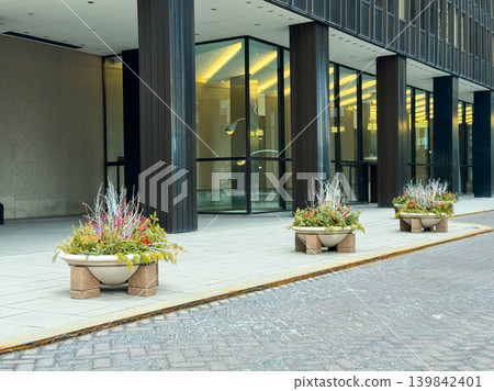 Planters display plants in front of building on city street during daytime with clear skies Planters display plants in front of building on city street during daytime with clear skies 139842401