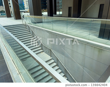 Steps lead down from a modern building with glass railings in an urban area during the daytime Steps lead down from a modern building with glass railings in an urban area during the daytime 139842404