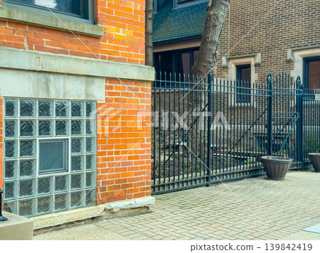 Brick wall and metal fence near building with glass block window in urban area during daytime hours with clear skies Brick wall and metal fence near building with glass block window in urban area during daytime hours with clear skies 139842419