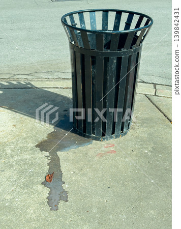 Trash can on the street with a puddle of water nearby during a sunny day in a city 139842431