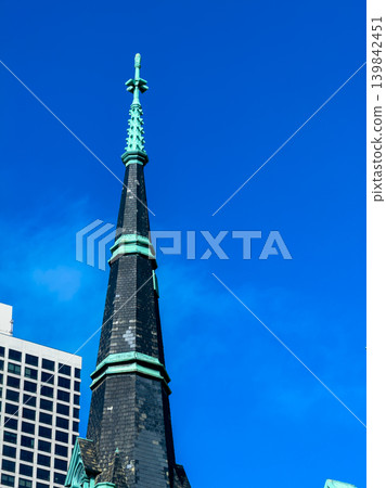 Tall church steeple reaches towards the blue sky over a city skyline on a sunny day in the afternoon 139842451