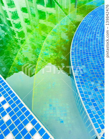 Water reflections show blue tiles and green hues in a pool area during midday in a residential complex Water reflections show blue tiles and green hues in a pool area during midday in a residential complex 139842476