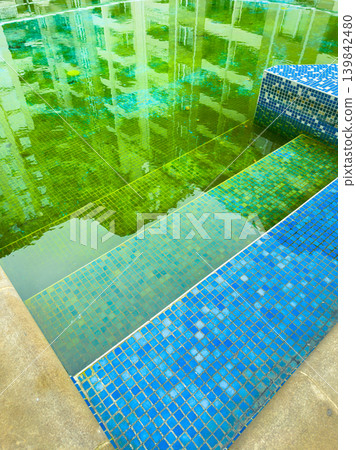 Green water and blue tiles in a swimming pool area during the day in a residential building setting Green water and blue tiles in a swimming pool area during the day in a residential building setting 139842480