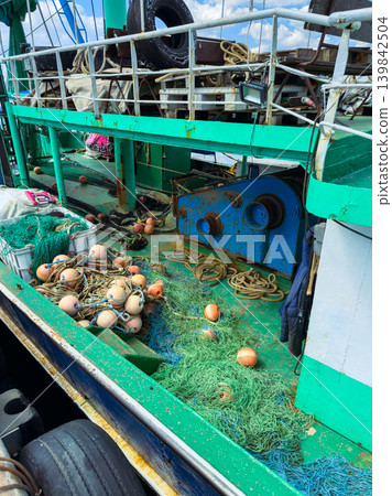 Fishing boat deck shows equipment and materials used for catching fish and handling nets during a sunny day at sea in an unspecified location Fishing boat deck shows equipment and materials used for catching fish and handling nets during a sunny day at sea in an unspecified location 139842504