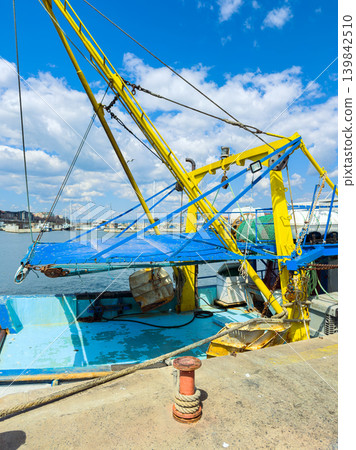 Fishing boat docked at a harbor under a clear sky with clouds and equipment ready for work Fishing boat docked at a harbor under a clear sky with clouds and equipment ready for work 139842510