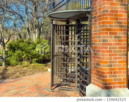 Metal turnstile located near a brick structure with trees and bushes, capturing a busy park scene during daytime hours Metal turnstile located near a brick structure with trees and bushes, capturing a busy park scene during daytime hours 139842523