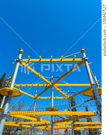 Sky view of a yellow structure at a playground in a park during a sunny day with clear blue sky, showing metal beams and supports 139842527