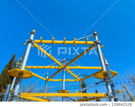 Construction site with a yellow support structure and blue sky visible above, showing metal beams and safety fence during daytime Construction site with a yellow support structure and blue sky visible above, showing metal beams and safety fence during daytime 139842528