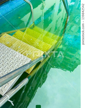 Steps lead into a green pool under a clear sky in an urban area during daytime Steps lead into a green pool under a clear sky in an urban area during daytime 139842542