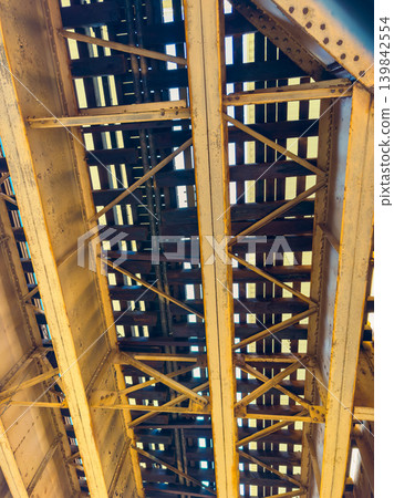Steel beams and wooden slats form a bridge structure under a clear sky in an urban area during daylight hours Steel beams and wooden slats form a bridge structure under a clear sky in an urban area during daylight hours 139842554