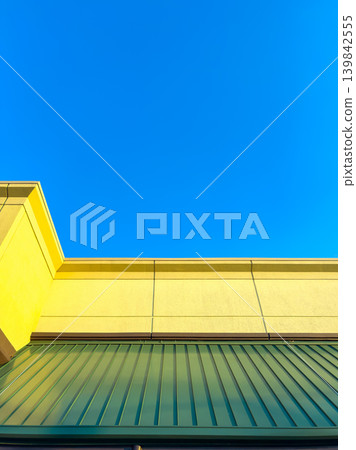 Bright yellow wall and green awning under clear blue sky during daytime in an urban area in the summer season Bright yellow wall and green awning under clear blue sky during daytime in an urban area in the summer season 139842555
