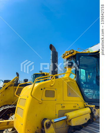 Heavy machinery is parked under a clear blue sky at a construction site during daytime hours in an open area 139842558