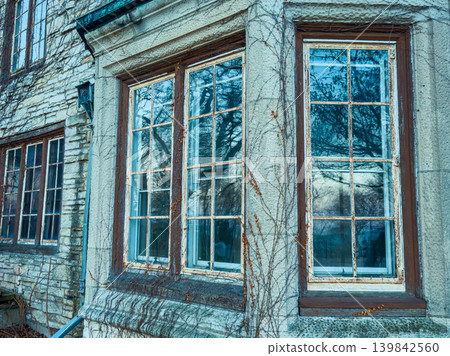 Old house windows show signs of age with vines growing on the walls during late afternoon light Old house windows show signs of age with vines growing on the walls during late afternoon light 139842560