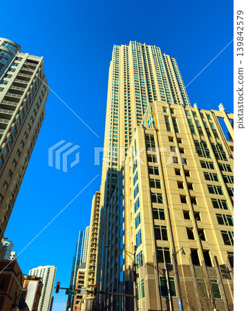Tall buildings reach for the blue sky in a bustling city center during a bright day, showcasing modern architecture and urban life Tall buildings reach for the blue sky in a bustling city center during a bright day, showcasing modern architecture and urban life 139842579