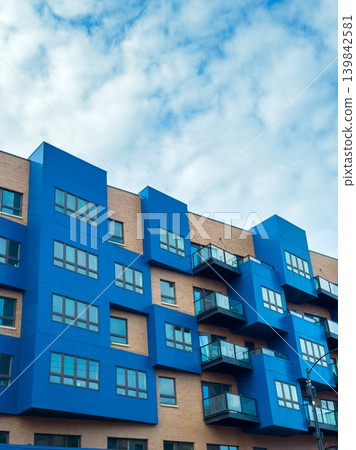 Tall blue apartment building with balconies under a cloudy sky in an urban area during daytime hours Tall blue apartment building with balconies under a cloudy sky in an urban area during daytime hours 139842581