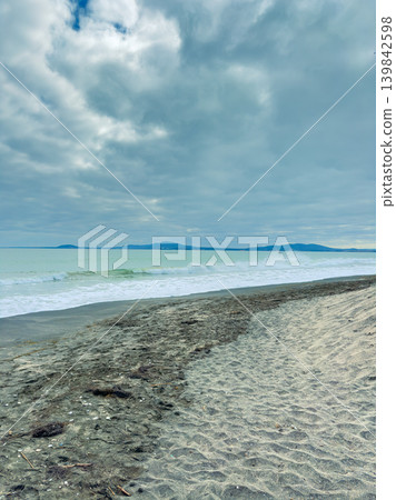 Cloudy day at the beach with waves and distant mountains in the background near the shore Cloudy day at the beach with waves and distant mountains in the background near the shore 139842598