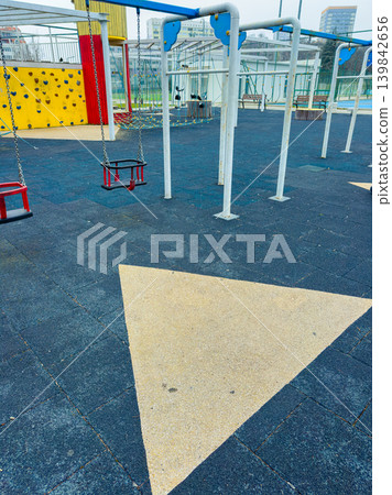 Playground with swings and climbing wall in a city park during a cloudy day 139842656