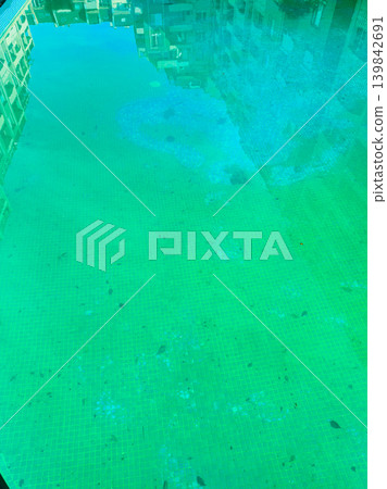 Clear water in a pool reflects buildings nearby during daytime showing a bright green color with some fish swimming under the surface Clear water in a pool reflects buildings nearby during daytime showing a bright green color with some fish swimming under the surface 139842691