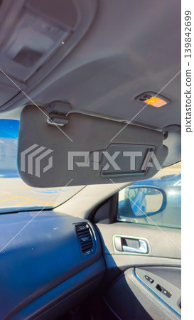Sun visor in car interior showing functionality in bright daylight while vehicle is parked in a shopping area Sun visor in car interior showing functionality in bright daylight while vehicle is parked in a shopping area 139842699