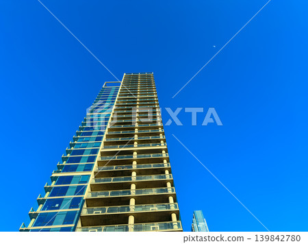 Tall building reaches towards clear blue sky in urban area during daytime with a hint of moon in the background Tall building reaches towards clear blue sky in urban area during daytime with a hint of moon in the background 139842780