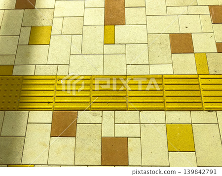 Yellow tactile paving on sidewalk in urban area designed for better accessibility while people walk along the street 139842791