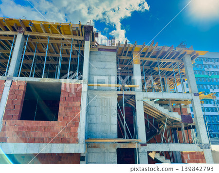 Construction project in progress at a building site with scaffolding and brickwork in a city under a bright blue sky Construction project in progress at a building site with scaffolding and brickwork in a city under a bright blue sky 139842793