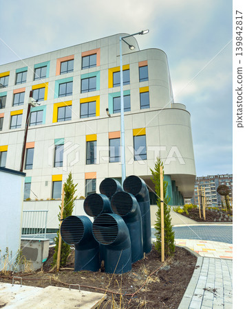 Modern building with ventilation pipes outside near colorful windows on an overcast day in a city Modern building with ventilation pipes outside near colorful windows on an overcast day in a city 139842817