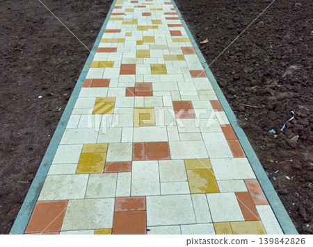 Pathway made of square tiles leads through bare soil in a garden area during a cloudy day in autumn Pathway made of square tiles leads through bare soil in a garden area during a cloudy day in autumn 139842826