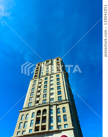 Tall building reaches into blue sky in urban area during afternoon with few clouds present and sunlight shining brightly 139842851