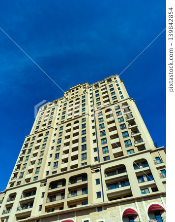 Tall building stands under blue sky in a busy city area during the afternoon 139842854