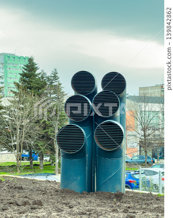 Construction site shows large ventilation pipes near buildings and trees under cloudy sky during daytime hours in an urban area Construction site shows large ventilation pipes near buildings and trees under cloudy sky during daytime hours in an urban area 139842862