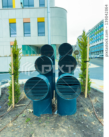 Ventilation pipes arranged in a row next to a modern building in an urban setting during daytime hours Ventilation pipes arranged in a row next to a modern building in an urban setting during daytime hours 139842864