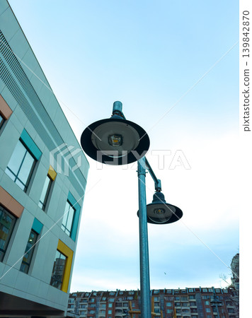 Street lamps stand tall near a modern building as clouds gather in the overcast sky during late afternoon in the city 139842870