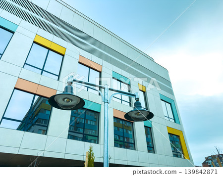 Modern building with colorful windows and street lamps seen from below on a cloudy day in an urban area with architectural details Modern building with colorful windows and street lamps seen from below on a cloudy day in an urban area with architectural details 139842871