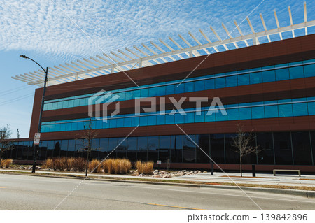Modern building with glass facade located along a city street on a clear day with blue sky and clouds during afternoon Modern building with glass facade located along a city street on a clear day with blue sky and clouds during afternoon 139842896